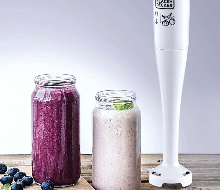 A parent using the Black+Decker SB2500-B5 stick blender to quickly and smoothly puree baby food or pureed fruit in a small cup.