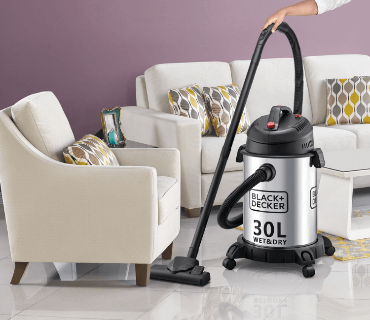 Black+Decker WV1450-B5 heavy-duty vacuum cleaner in a workshop or garage, showcasing its durable wheels and large capacity for industrial use.
